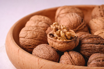 Walnuts heap food in wooden bowl on white background with half peeled nut, angle view, healthy food concept