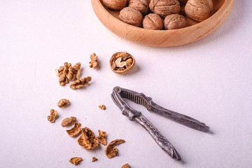 Walnuts heap food in wooden bowl with half peeled nut, cracked nutshell, near to vintage nutcracker on white background, angle view, healthy food concept