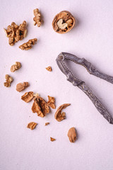 Walnuts heap food with half peeled nut, cracked nutshell, near to vintage nutcracker on white background, top view, healthy food concept