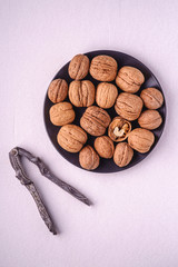 Walnuts heap food with half peeled nut in black plate near to vintage nut cracker on white background, top view, healthy food concept