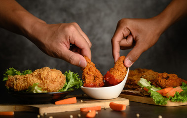 Two hand holding crispy fried chicken dipped in tomato sauce