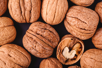 Walnuts heap food in black plate with half peeled nut, texture, top view, healthy food concept