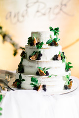 Naked wedding cake. White four-tiered wedding rustic cake with berries and figs and greenery, on the background of white arch