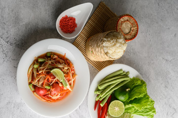 Thai papaya salad in a white plate with Sticky rice in wicker basket bamboo and dried shrimp.