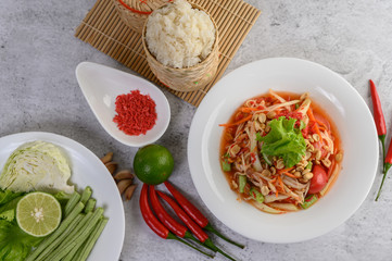 Thai papaya salad in a white plate with Sticky rice in wicker basket bamboo and dried shrimp.