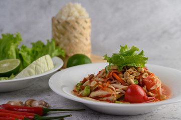 Thai papaya salad in a white plate with Sticky rice in wicker basket bamboo, lime, and chili