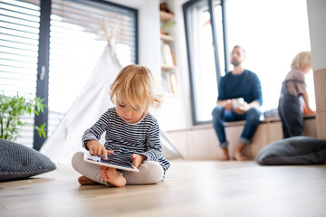 Cute small toddler girl indoors in bedroom playing with tablet. - Powered by Adobe