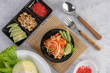 Thai papaya salad in a white plate with Spoon, fork, and dried shrimp.