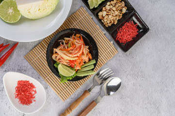 Fototapeta na wymiar Thai papaya salad in a white plate with Spoon, fork, and dried shrimp.