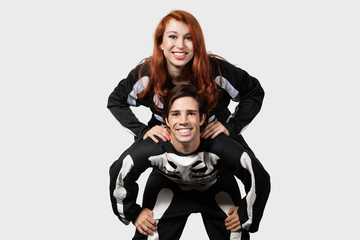 Portrait of young man giving piggyback ride in skeleton costume over gray background