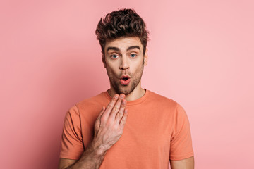 Obraz premium shocked man holding hand near mouth while looking at camera on pink background