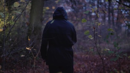 A man in a hood with a flashlight in his hand walks through a dark forest. Search for a man