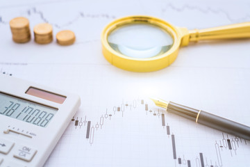 Calculator, magnifying glass, coins and pen on a bar chart-stock finance concept image