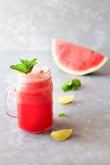 Watermelon smoothie with mint leaves and lemon slices on a gray wooden background.