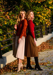 colorful fall forest. real femininity. autumn women outdoor. girl friends walk in park. sunny day with leaves. fall fashion season. Pleated trend. girls in corrugated skirt and sweater. female beauty