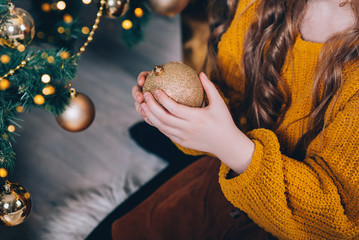 Little girl decorating Christmas tree with golden toys.