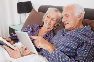 Happy senior couple using digital tablet while lying on bed in room