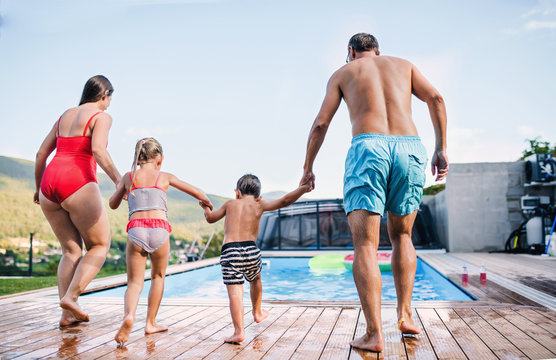 Rear view of family with two small children by swimming pool outdoors.