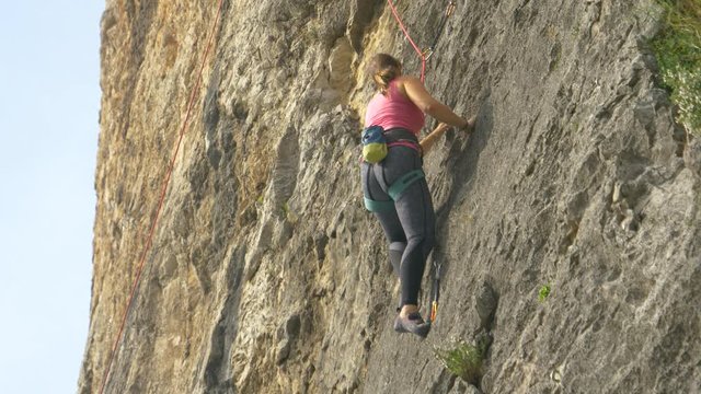 CLOSE UP: Young Caucasian woman goes rock climbing up a mountain in Slovenian countryside. Experienced female rock climber makes her way up a rocky wall. Hobby rock climber scales a towering cliff.