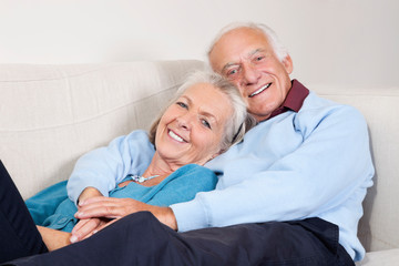 Portrait of happy elderly man with arm around spouse lying on sofa at home