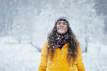 Happy girl in yellow jacket throws snow up in winter forest.