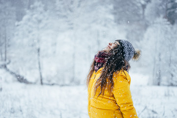 Happy girl in yellow jacket throws snow up in winter forest.