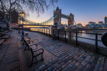 Tower Bridge with bench and street lamp foreground during sunrise, London, UK
