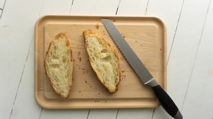 Cut croissant on a wooden cutting board with bread knife near it. White wooden background