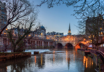 Pulteney Bridge with reflection in Avon river with dry tree foreground during twilight at Bath, UK