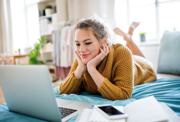 Young woman with laptop lying on bed indoors at home, relaxing. - Powered by Adobe