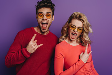 excited man and woman showing rock signs on purple background