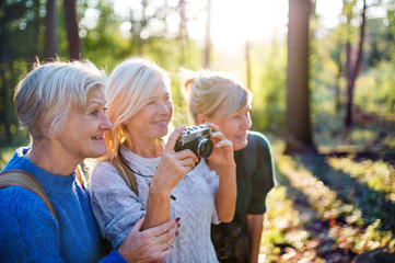 Senior women friends walking outdoors in forest, taking photos with camera.