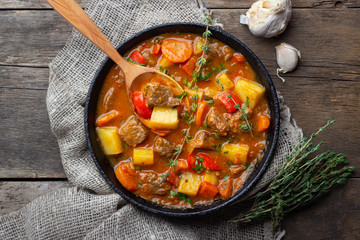 Goulash, beef stew or bogrash soup with meat, vegetables and spices in cast iron pan on wooden...