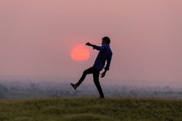 Silhouette of a man jumping in front of the sun during sunset