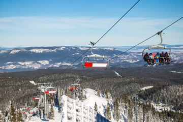 Six-seat mountain ski lift in winter. Behind you can see the pine forests and mountains covered with snow.