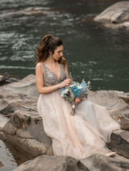 Fototapeta na wymiar Beautiful brunette bride in light chiffon wedding dress embroidered with beads posing near the mountains. Wedding in Carpathian Mountains. Romantic beautiful bride in luxury dress posing outdoors