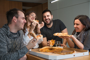 Friends having fun while eating pizza at home