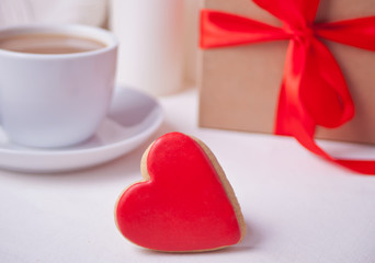 Heart shaped red cookie with gift box and cup of coffee on the white table