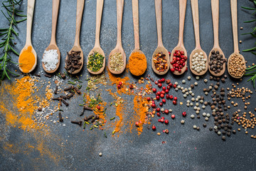 Colourful various herbs and spices in spoons for cooking on dark background