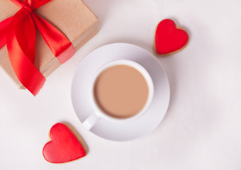 Obraz na płótnie Canvas Cup of coffee and a heart shaped red cookies with gift box on the white table