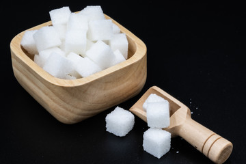 White sugar cube in wooden cup on black background.