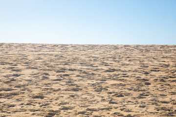 Blue sky over a golden yellow sand dune with a lot of structures and shapes close to a beach where pople enjoy a sunbath and their holiday vacation travel