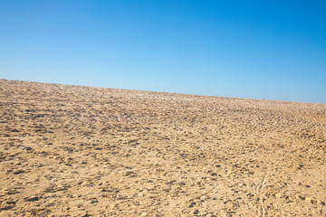 Blue sky over a golden yellow sand dune with a lot of structures and shapes close to a beach where pople enjoy a sunbath and their holiday vacation travel