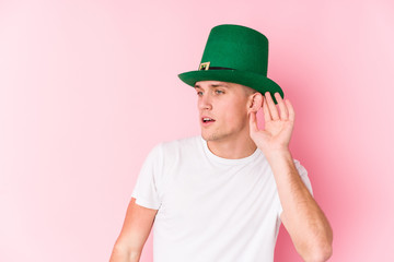 Young caucasian man celebrating saint patricks day trying to listening a gossip.