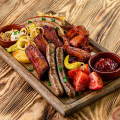 grilled meat set on a wooden table, ribs, sausages, wings and vegetables with sauce