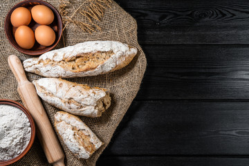 flour in a wooden bowl on dark wooden background with spikelets of wheat, eggs, milk and butter, top view with copy space.