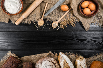 flour in a wooden bowl on dark wooden background with spikelets of wheat, eggs