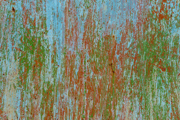 Old painted scratched streaked metal surface. Several layers of paint are visible: brown, green, blue. Abstract colorful texture background