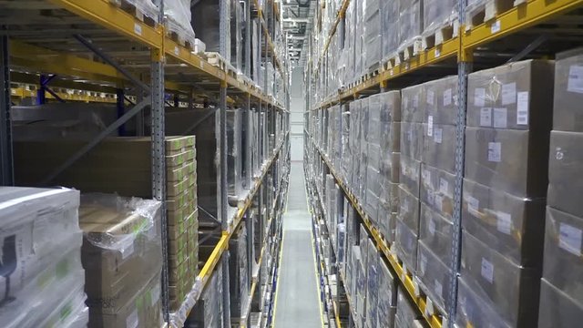 Motion view of packages and boxes in interior of industrial warehouse at factory. Cardboard and plastic packaging with products are on high shelves in storehouse of modern plant during working day