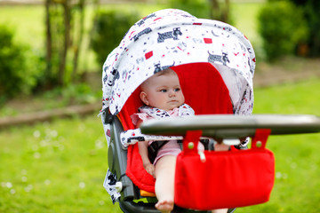 Cute little beautiful baby girl of 6 months sitting in the pram or stroller and waiting for mom. Happy smiling child with blue eyes